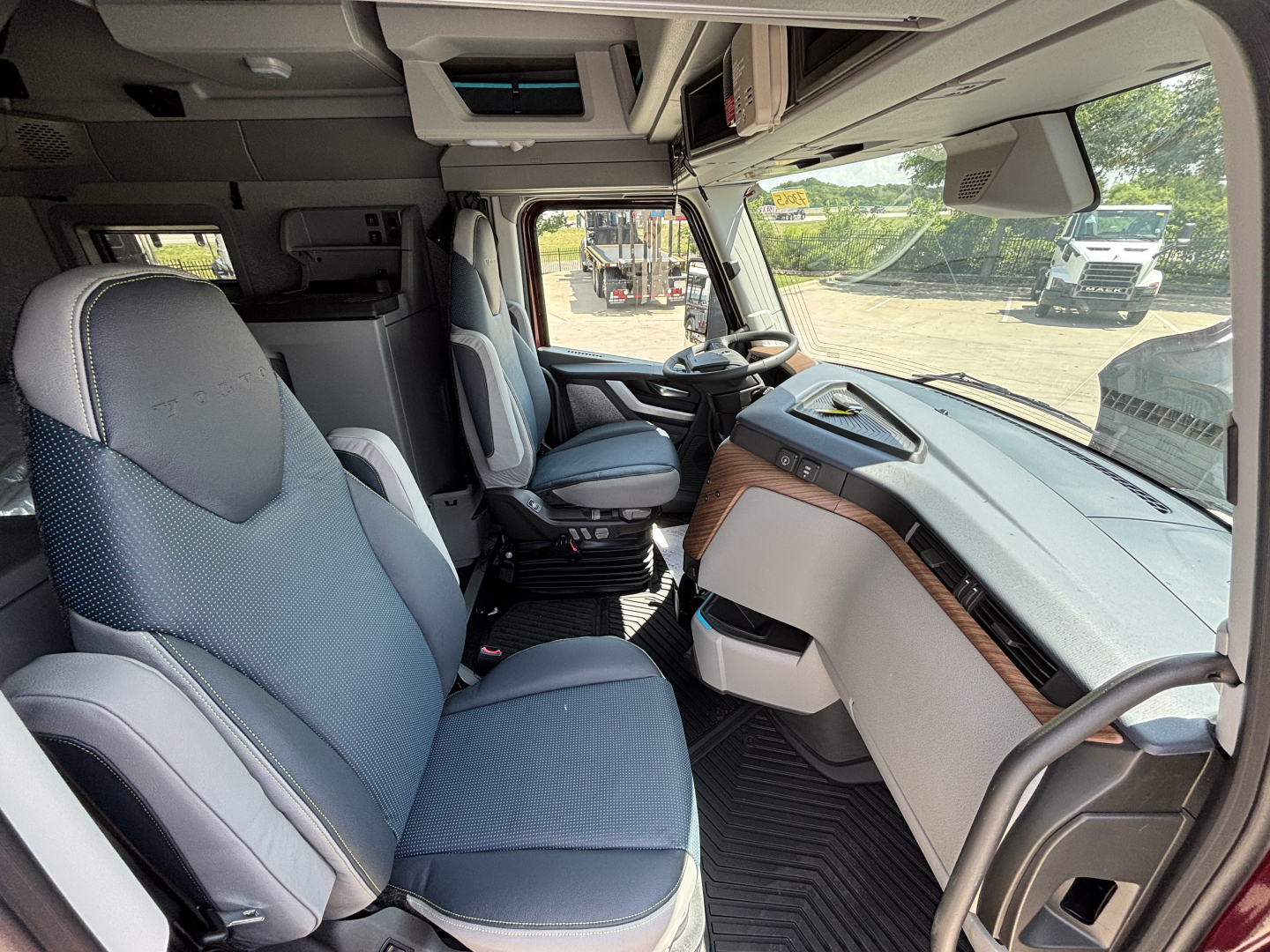 Volvo VNL-64T-860 truck cabin interior showing driver and passenger seats, dashboard with wood trim, overhead console, and steering wheel.