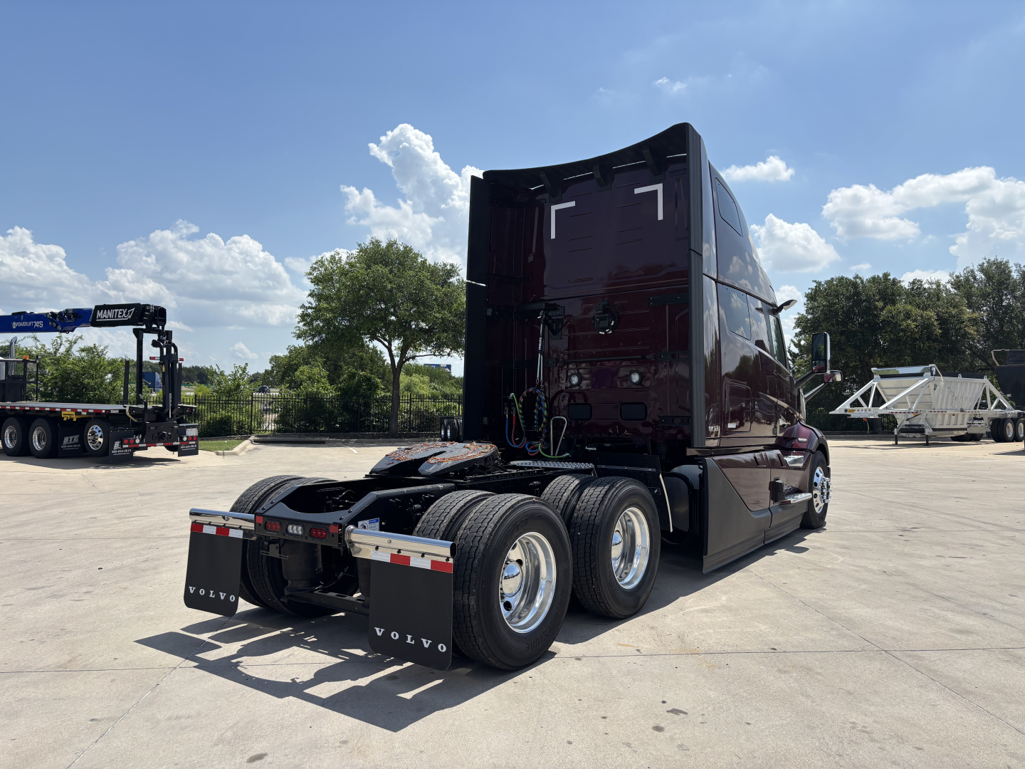 Volvo VNL64T860 tractor-trailer cab from rear quarter showing third-axle configuration and fifth wheel; glossy dark maroon paint with Volvo rear mud flaps and chrome wheels.