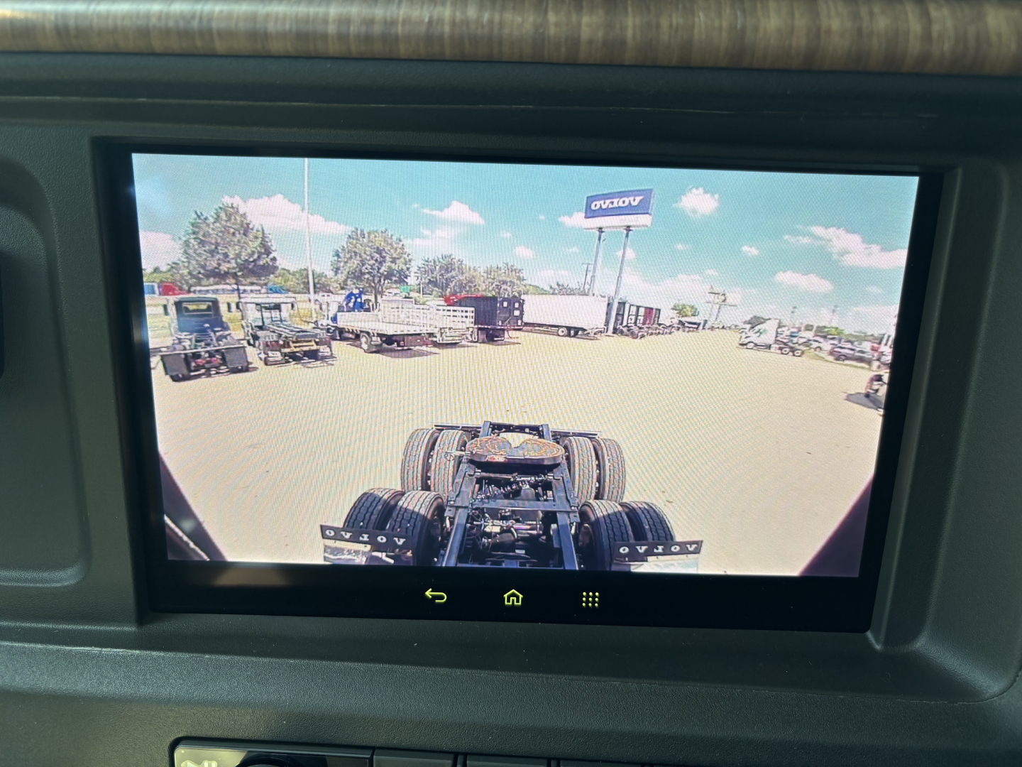 In-vehicle rear view camera display showing tractor-trailer cab chassis and rear wheels in view.