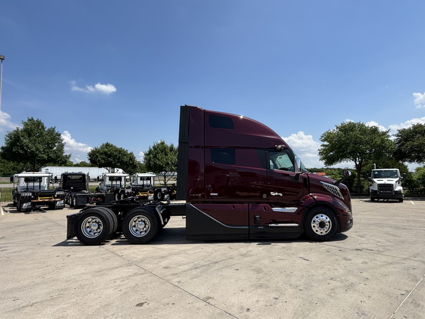 Volvo VNL64T860 truck side view showing cab with maroon paint and 6x4 rear wheels in a dealership lot