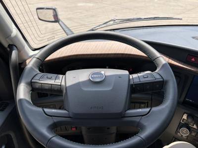 Volvo truck steering wheel in-cab view showing steering wheel with Volvo logo and control buttons.