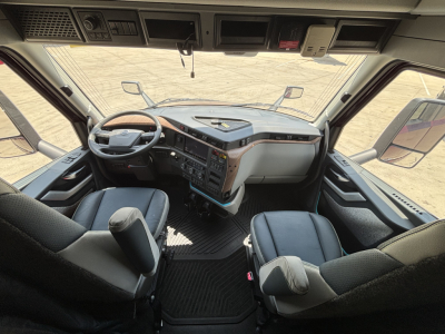 Cab interior of a 2027 Volvo VNL64T860 tractor showing steering wheel, dashboard, and two seats with controls and overhead compartments.