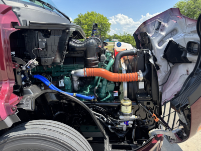Volvo VNL64T860 engine bay view showing green engine, orange coolant hose, black air intake, and various hoses with front grille removed.