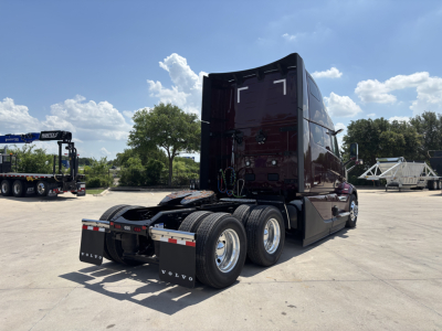 Volvo VNL64T860 tractor-trailer cab from rear quarter showing third-axle configuration and fifth wheel; glossy dark maroon paint with Volvo rear mud flaps and chrome wheels.