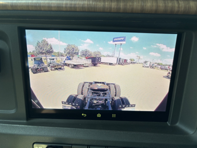 In-vehicle rear view camera display showing tractor-trailer cab chassis and rear wheels in view.
