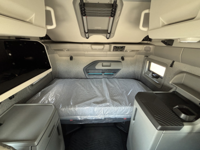 Volvo VNL64T860 sleeper cab interior showing bunk bed with plastic-covered mattress, overhead storage, scratchless panels, and side workspace in neutral tones.