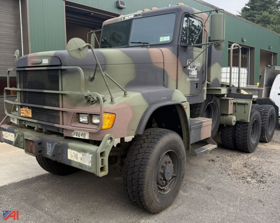 Freightliner M916A3 military tractor truck in camouflage, front-left angle, showing heavy-duty bumper, grille, headlights, and dual rear axles.