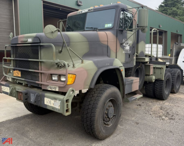 Freightliner M916A3 military tractor truck in camouflage, front-left angle, showing heavy-duty bumper, grille, headlights, and dual rear axles.