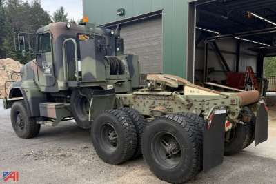 Military Freightliner M916A3 tractor showing crane cab and six-wheel rear, green camouflage paint, exposed drivetrain, and rear hook attachment.