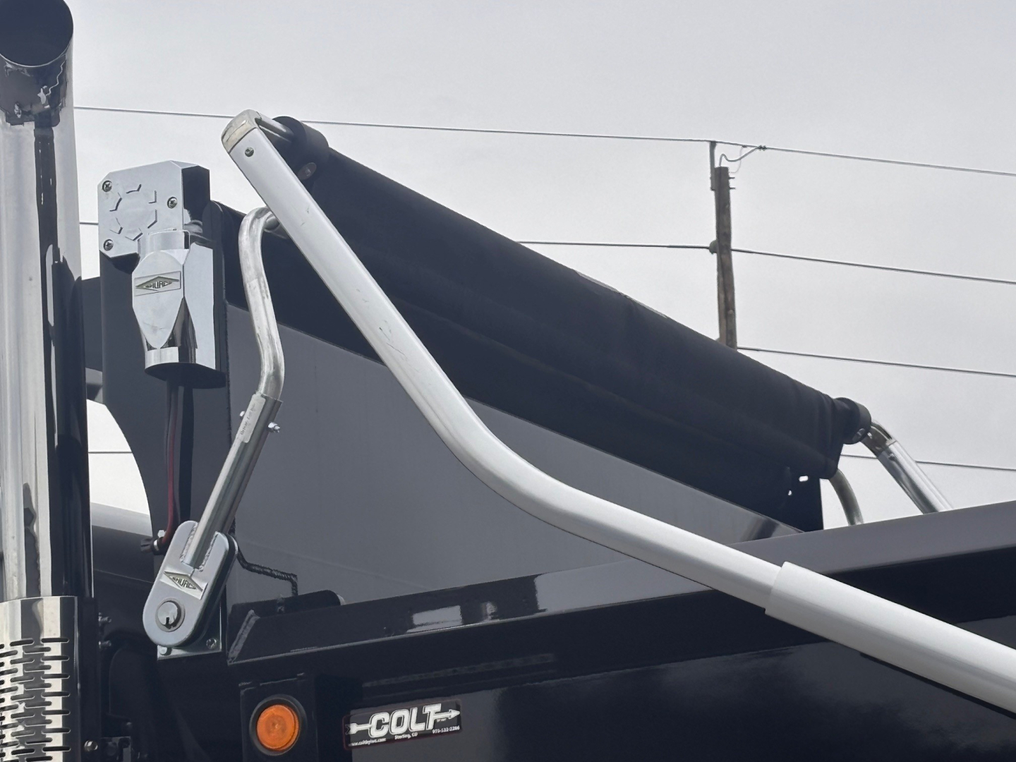 Truck part showing hydraulic lines and boom of a Mack PI64 dump truck with label 'COLT' on a component and control arm in view.