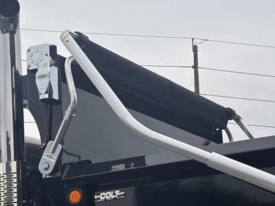Truck part showing hydraulic lines and boom of a Mack PI64 dump truck with label 'COLT' on a component and control arm in view.