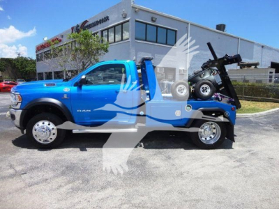 Blue Ram 4500 tow truck with winch, side view showing crane/boom and wheel tarps, dealership building in background.