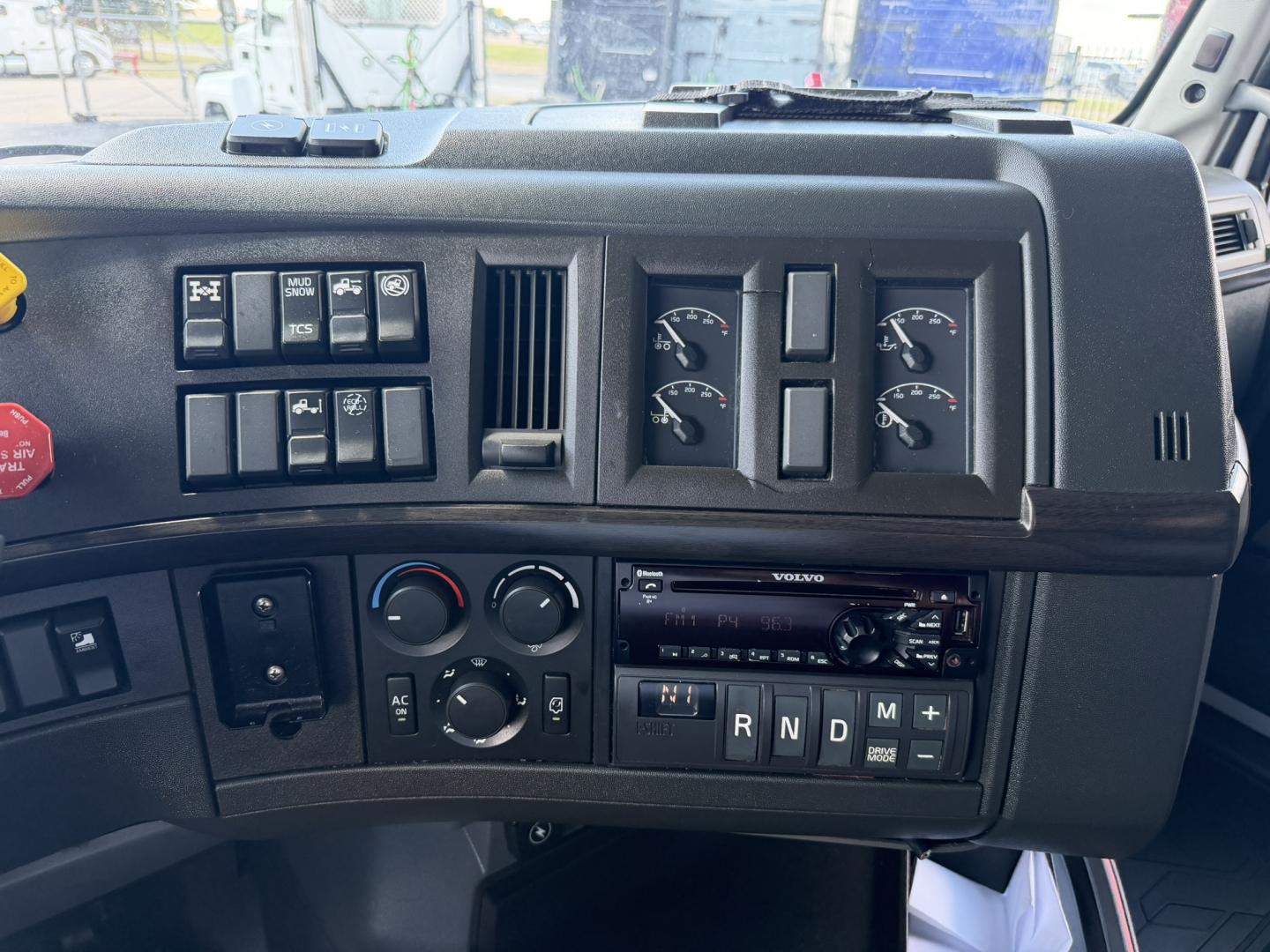 Volvo VNL64T740 truck dashboard cockpit with several gauges, controls, and a radio, showing climate controls and gear selector with R N D M positions.