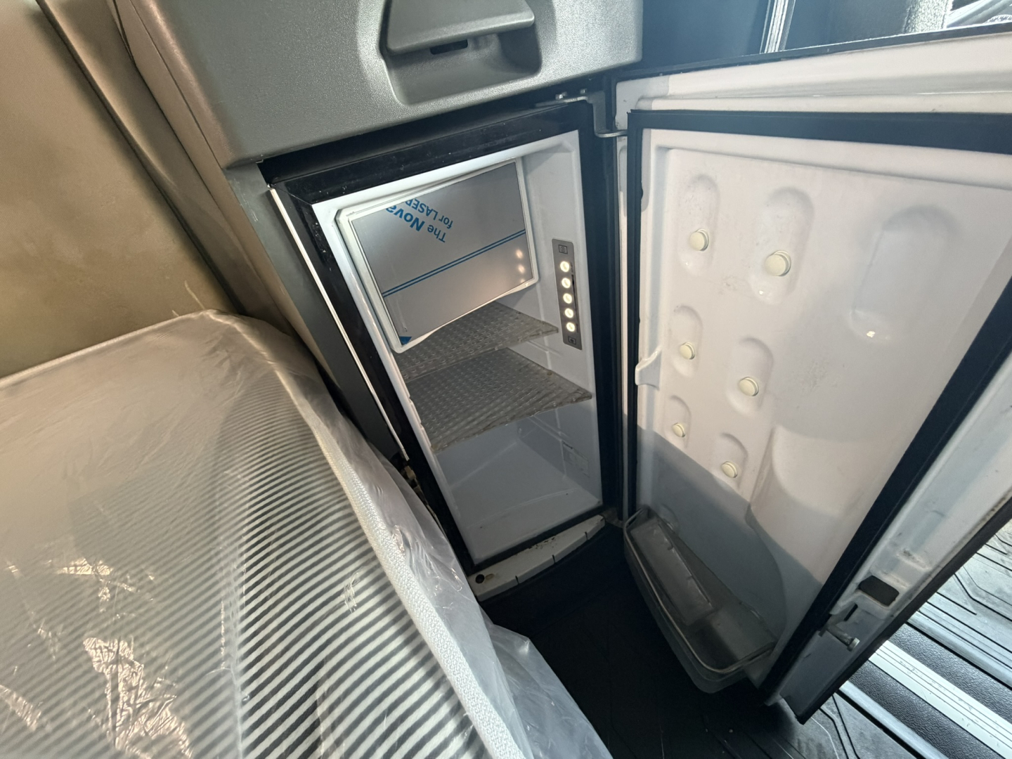 Ice blue mini fridge/freezer inside a Volvo VNL sleeper cab with door open; interior panels and base cabinet visible.