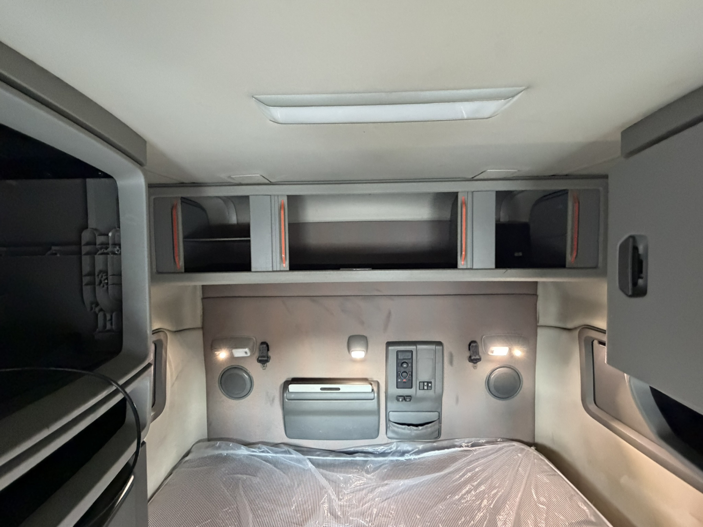 Interior sleeper cab rear wall of a Volvo VNL truck showing overhead storage shelves and control panel with two circular speakers and a vent.