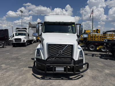Front view of a white Volvo VNL64T740 truck in a used-trucks lot with a black bull bar and grille guard, large chrome grille, daytime sky.