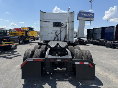 Truck rear view showing fifth wheel and rear chassis with mud flaps and taillights; Volvo dealership sign in background.
