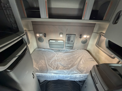 Interior sleeper cab of a Volvo VNL64T740 showing a bed with protective plastic, overhead storage, and control panel on the back wall.