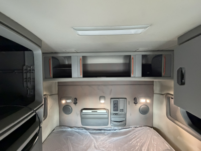Interior sleeper cab rear wall of a Volvo VNL truck showing overhead storage shelves and control panel with two circular speakers and a vent.