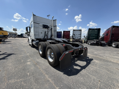 Truck chassis with a sleeper cab in background, dual rear wheels, mud flaps, and fifth wheel area visible.