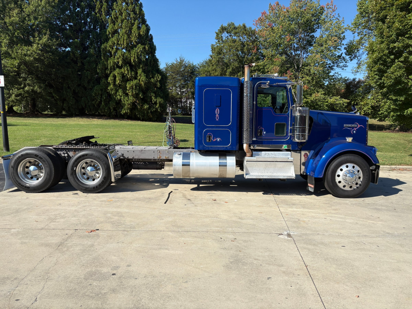 Kenworth W900L truck side view showing blue cab with chrome exhaust stack and fuel tank, extended chassis with triple rear axles.