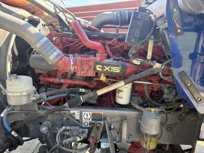 Kenworth W900L engine bay showing Cummins X15 label on valve cover and surrounding hoses and components.