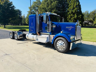 Kenworth W900L truck in blue profile view showing front grille, chrome bumper, side exhaust, and dual rear axles.