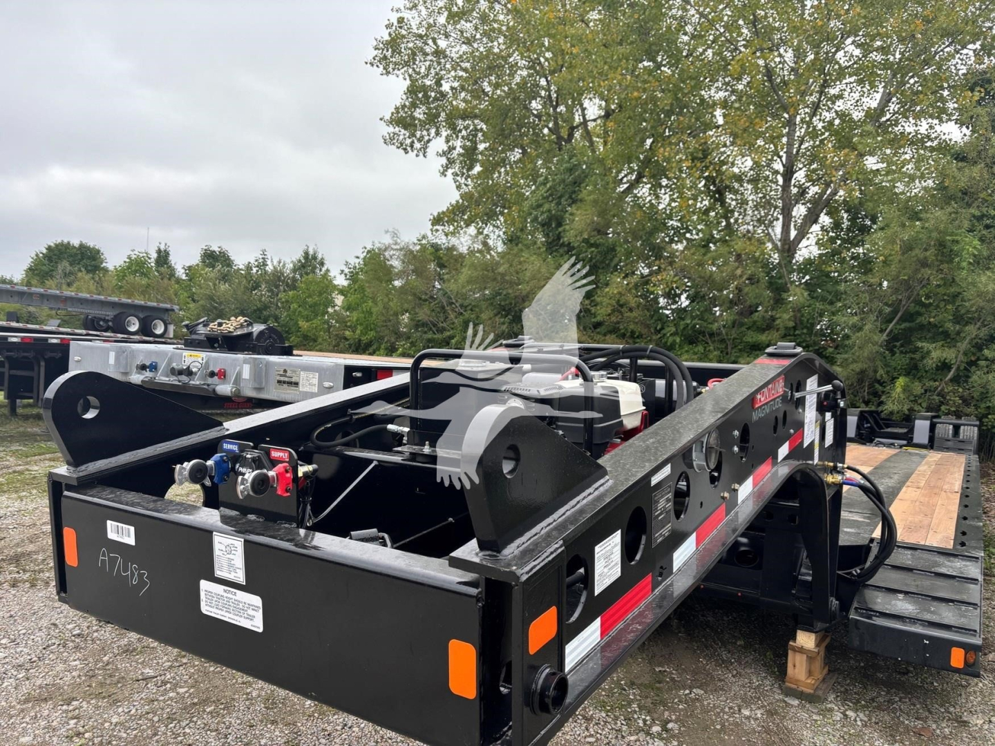 Fontaine 55MX lowboy trailer deck with black steel frame, hydraulic equipment visible, orange reflectors, white and red safety decals, VIN tag lacking legible text, stock number plate
