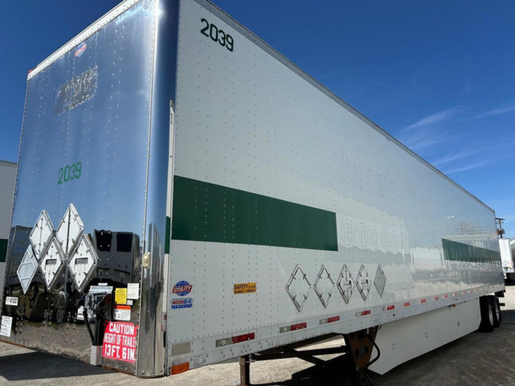 Trailer side view showing branding and safety decals. Visible text includes 2039 near front, hazard diamond stickers, and various small labels along lower edge.