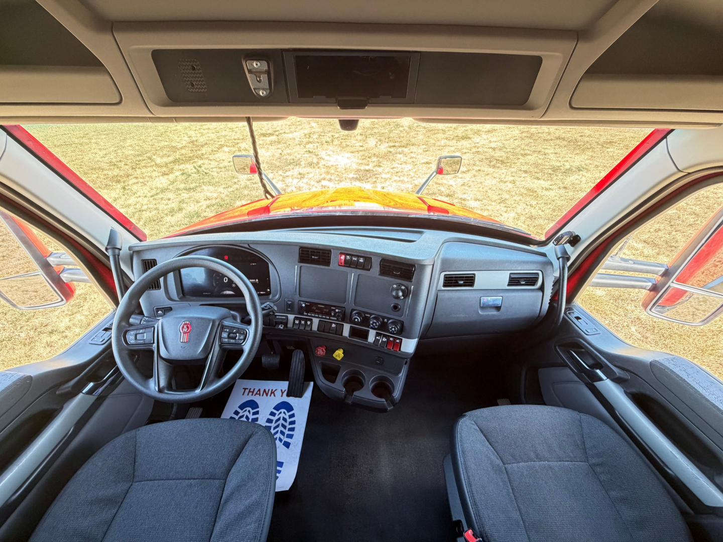 Kenworth T680 cabin interior from driver’s seat perspective showing steering wheel, dashboard, center console, and front seats.