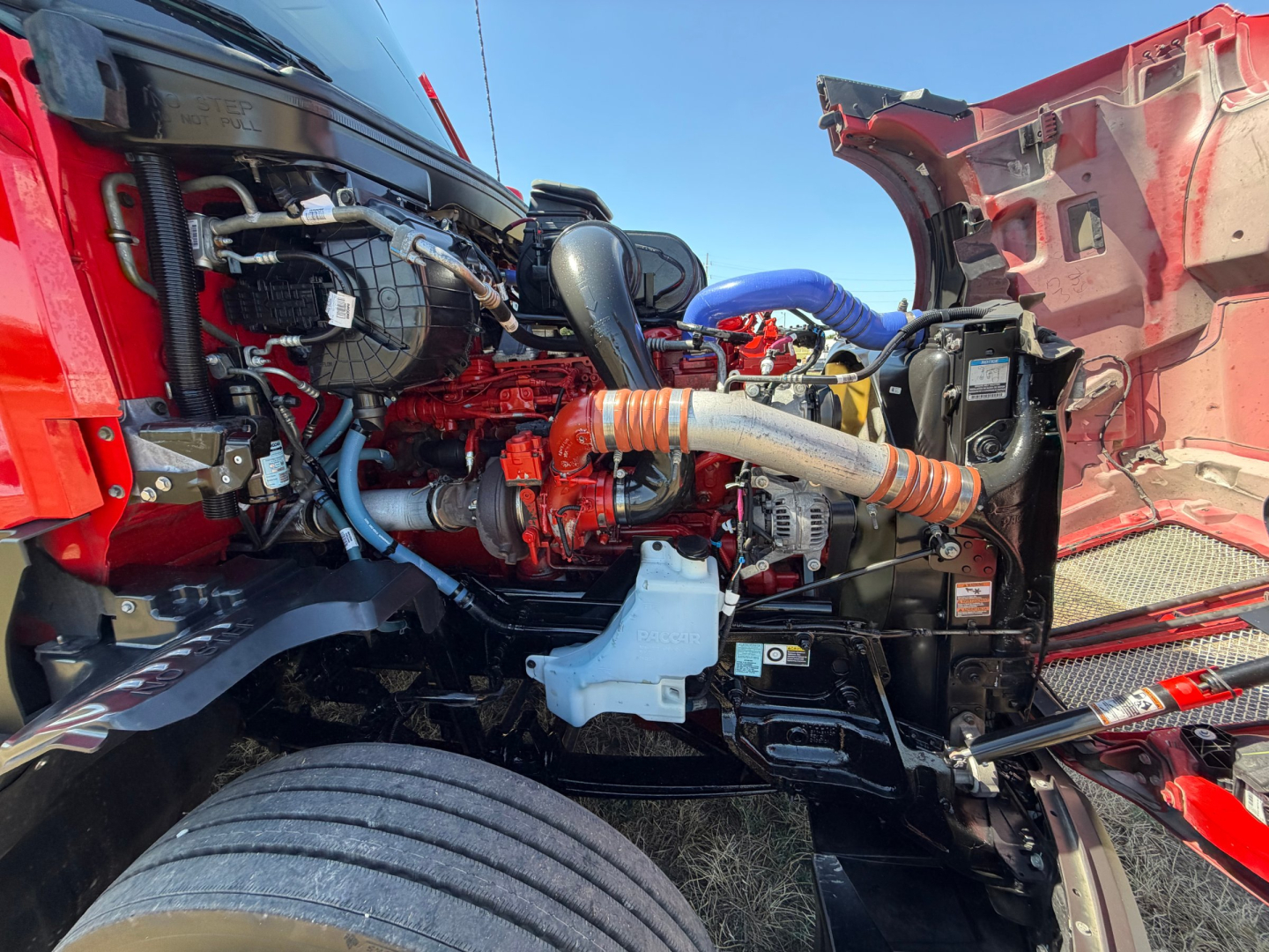 Kenworth T680 engine bay showing turbocharger and intercooler piping, hoses, coolant reservoir, and engine components visible through open hood.