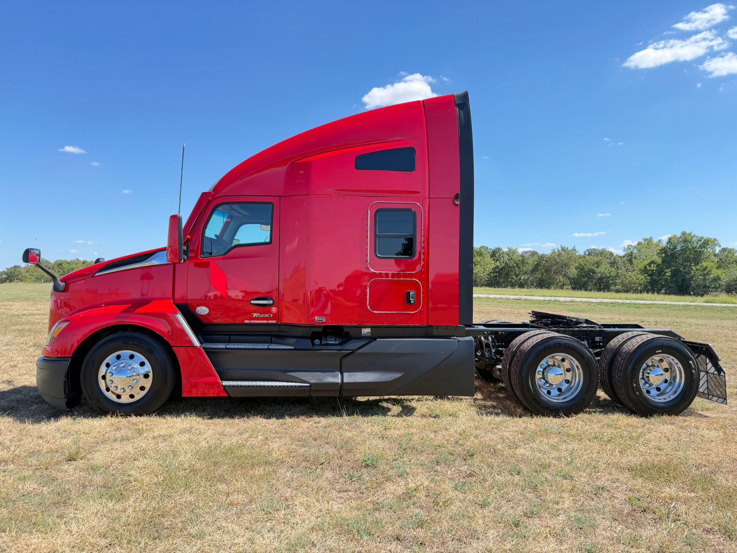 Kenworth T680 sleeper tractor in red side profile view with dual rear axles, chrome wheels, and field background.