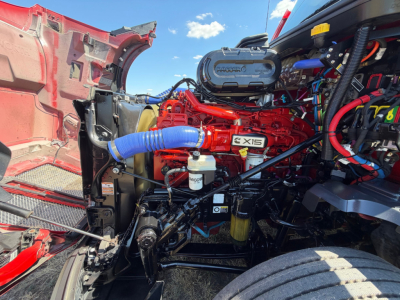 Kenworth T680 engine bay with red intake manifold, blue silicone hoses, Exis labeled component, and various wiring looms visible.