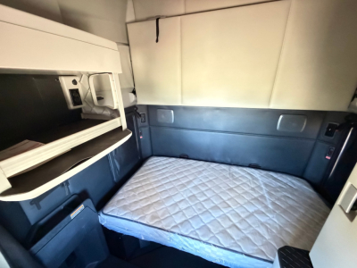 Kenworth truck sleeper cab interior with a bed and storage compartments. Mattress visible; side shelves and panels around the space.