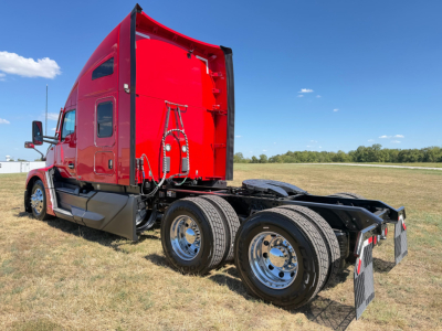 Kenworth T680 tractor in red color, side rear view showing tandem axles, sleeper cab, and exterior components.