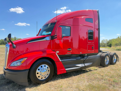 Kenworth T680 semi-truck cab side view in red, with sleeper, chrome wheels, dual rear axles, and clear sky.