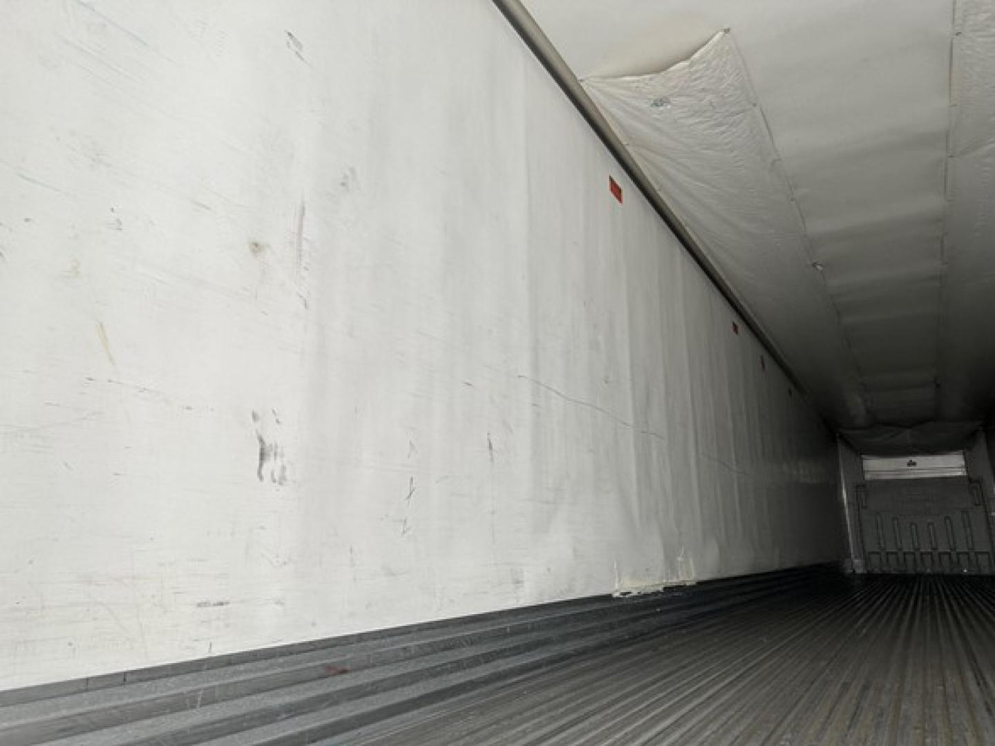 Trailer interior showing white sidewall and ribbed metal floor, empty cargo bay, overhead ceiling liner.