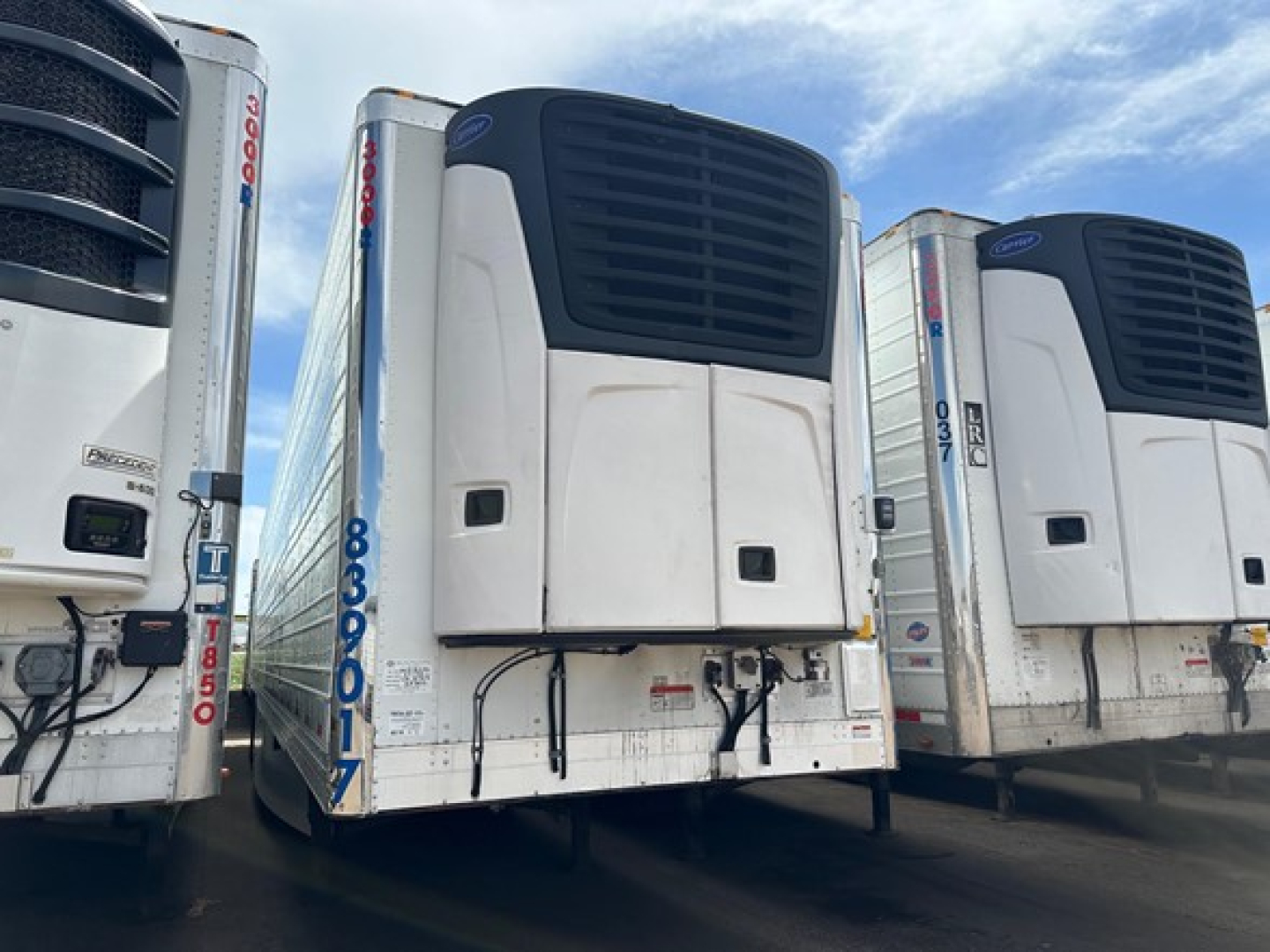 Trailer side view showing rear refrigeration unit on Utility 3000R trailer with vertical doors and white body. visible VIN plate area and blue identification numbers.