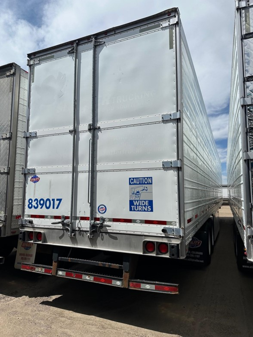 Rear view of a silver Utility air ride refrigerated trailer with doors closed, blue caution sticker, blue serial number 839017, and wide turns warning.