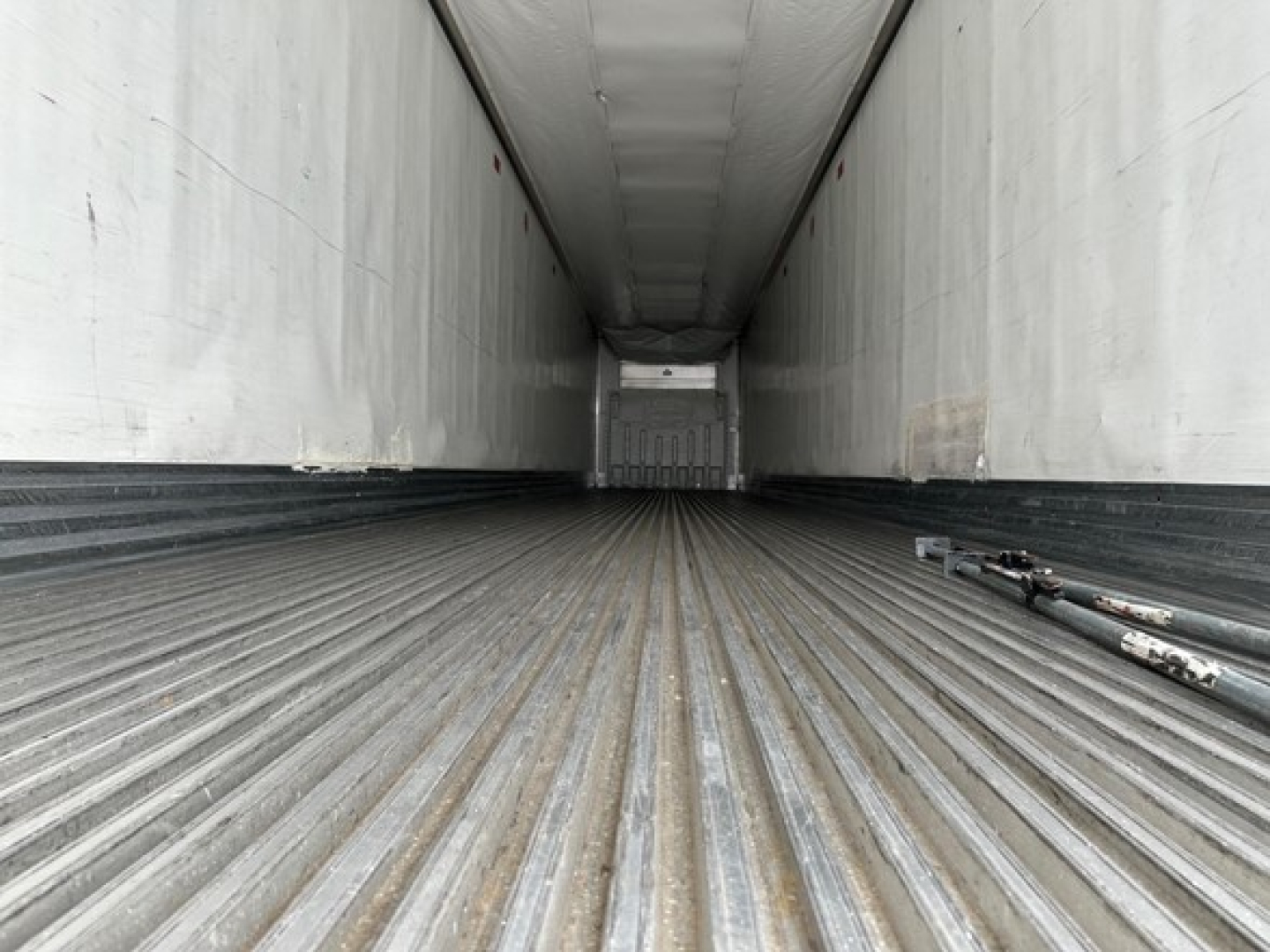 Trailer interior showing long aluminum cargo floor and sidewalls of a Utility Air Ride 3000R trailer, rear door at far end, no cargo, some hoses on floor.