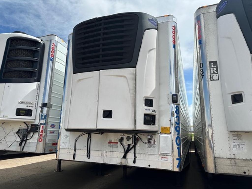 Unit showing a Utility 3000R refrigerated trailer with upright black vent on front, white refrigerated unit, side gates, and blue sky. Visible labels and serials include UE10818 and 2018 model.