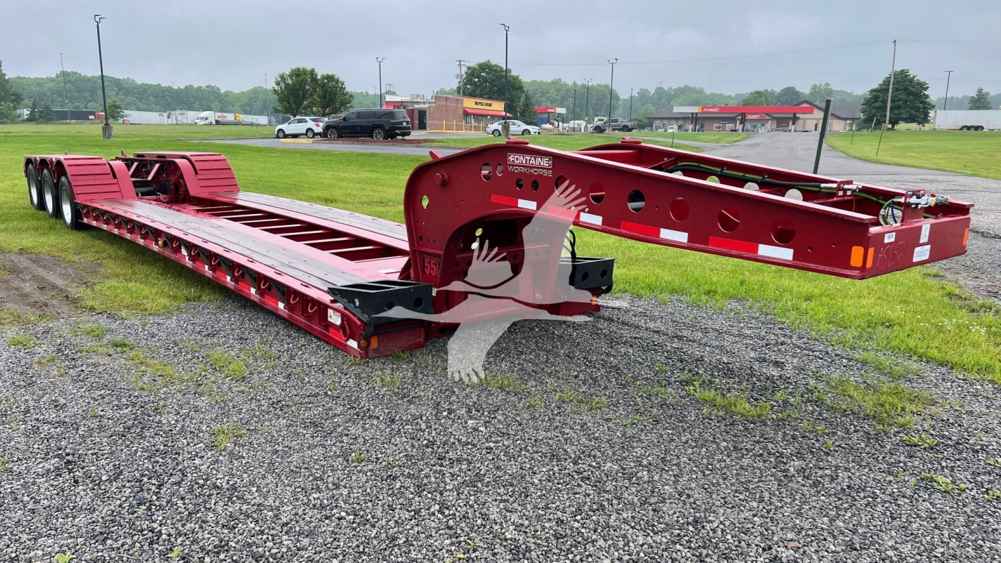 Fontaine 55 Lcc lowboy trailer showing red steel frame and long deck, viewed from front-right, with hitch and wheel sections visible.