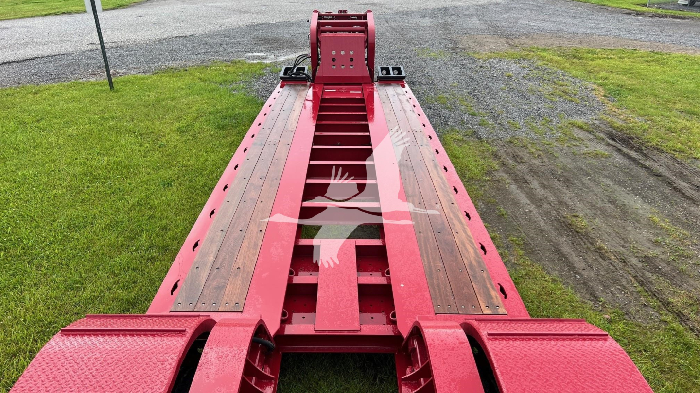 Lowboy trailer in red with extendable neck showing deck rollers and side rails.