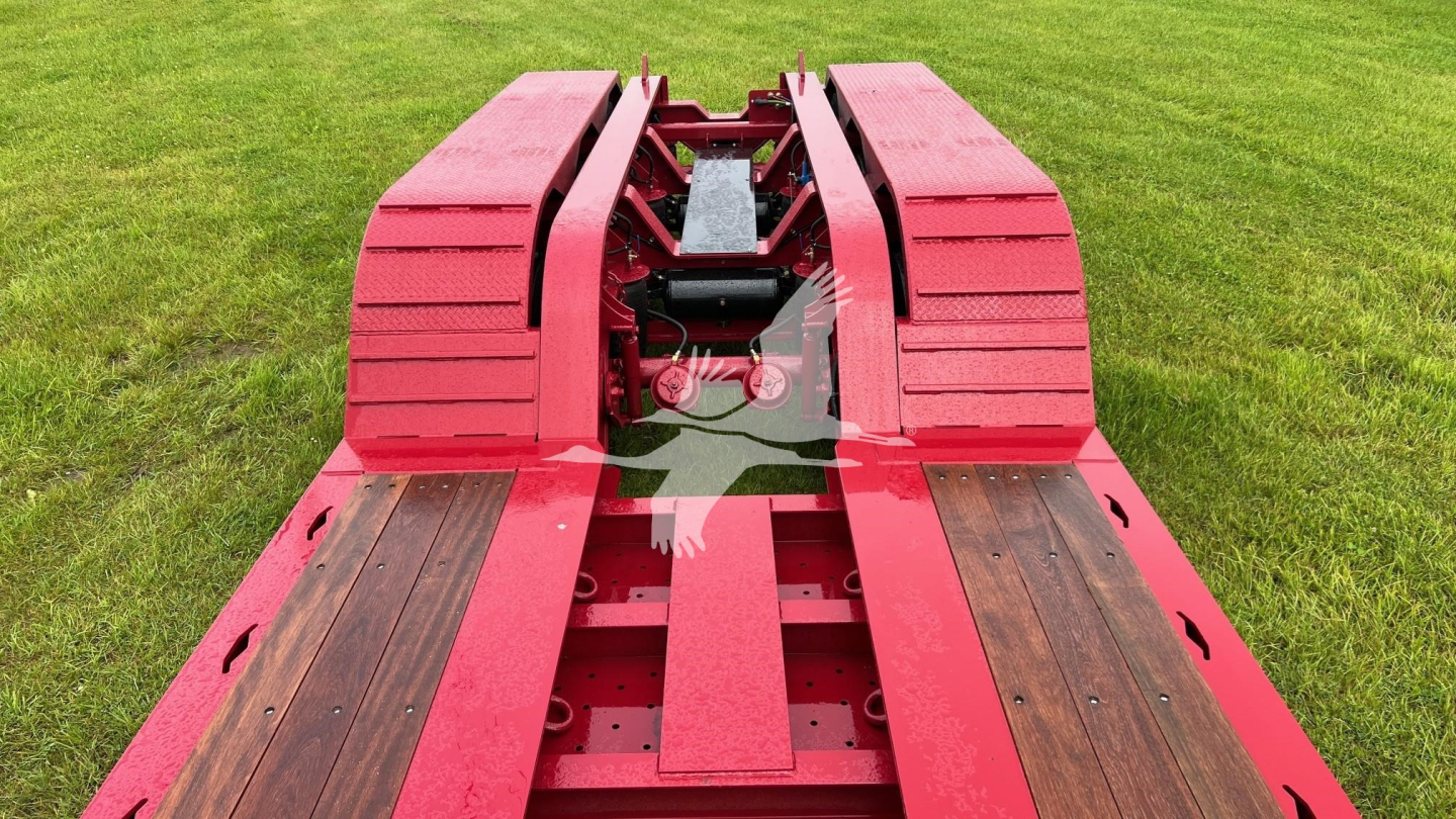 Lowboy trailer deck with red frame showing wooden planks and coupling area.