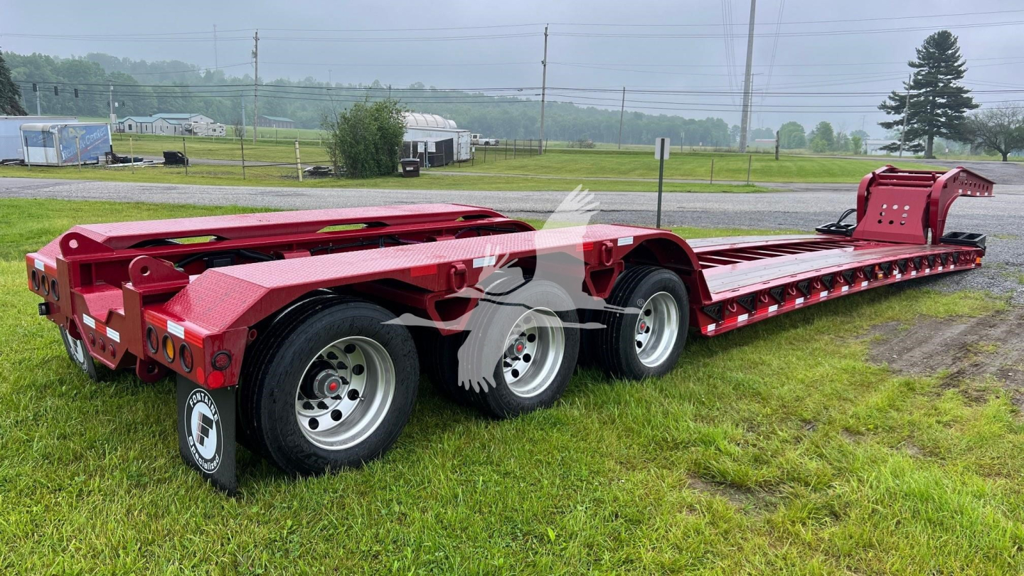 Trailer: Fontaine 55 Lowboy trailer viewed from rear-left showing long flatbed with multiple axles and red paint, wheel tires, and rear bumper area.