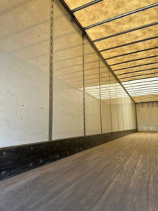 Trailer interior showing empty cargo area with wooden floor and side walls, vertical support tracks along left wall.