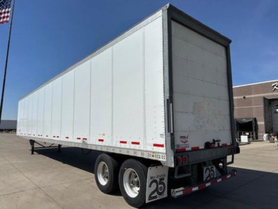 Trailer side and rear view showing a white enclosed van trailer with dual rear axles and minor dirt on rear doors. Visible are rear bumper, taillights, and reflective safety tape.