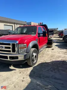 Ford F-550 crew cab dump truck in red with black bed sides, front grille and bumper, dual rear wheels, parked on a dirt lot with clear blue sky.