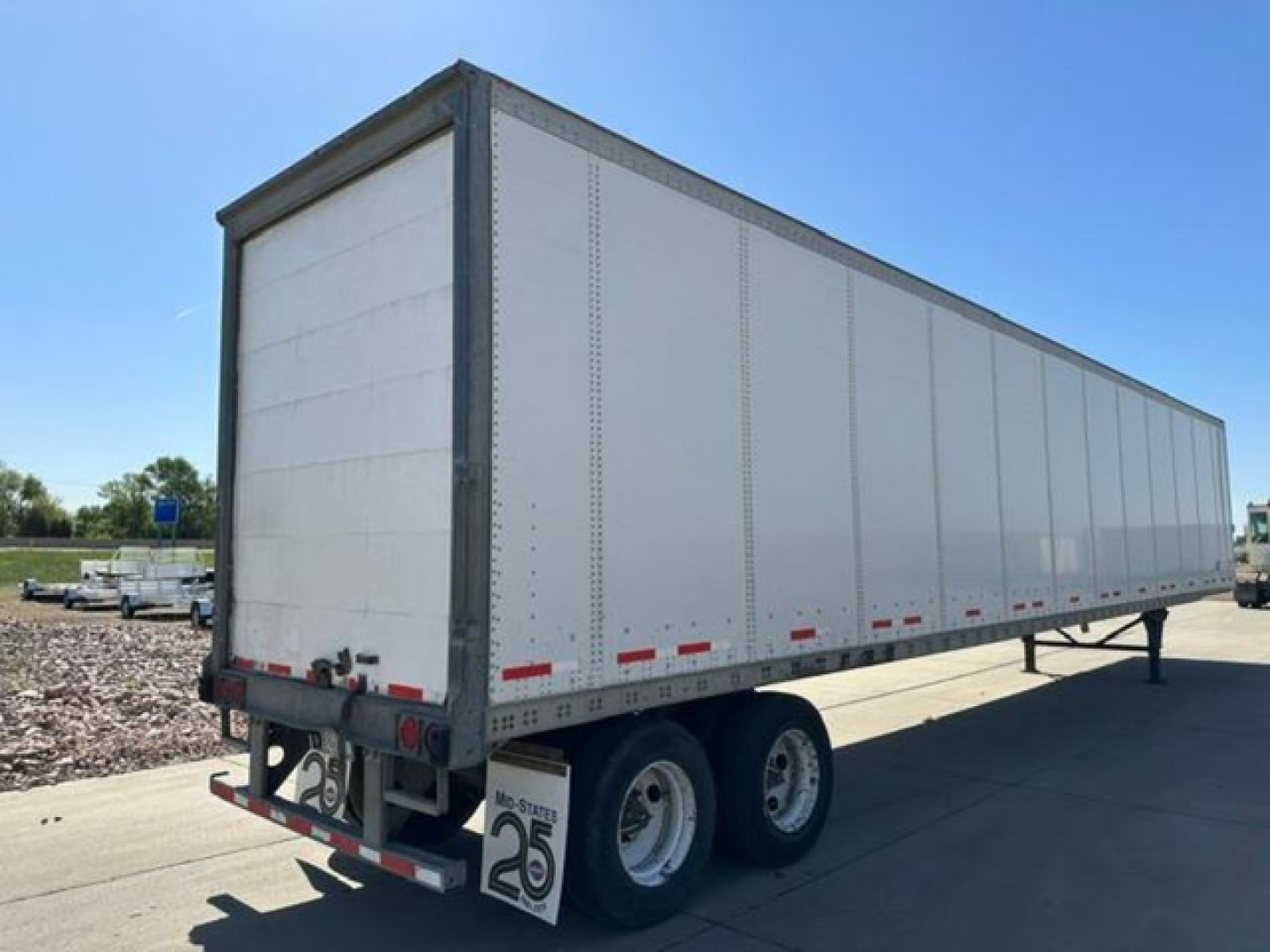 Trailer side view showing tandem axle semi-trailer with white aluminum walls and reflective red/white stripes.
