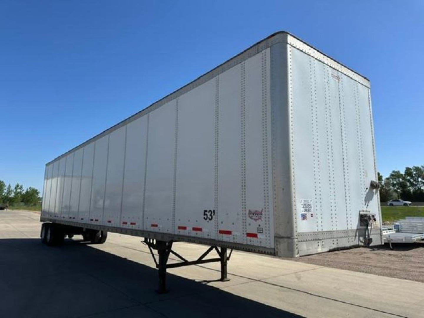 Trailer hitch and front corner of a 2014 Wabash van trailer viewed from the side, silver exterior, riveted aluminum sides, support legs down, rear doors.